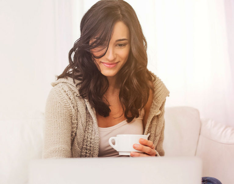 Brown haired woman sitting on couch with a white cup of tea